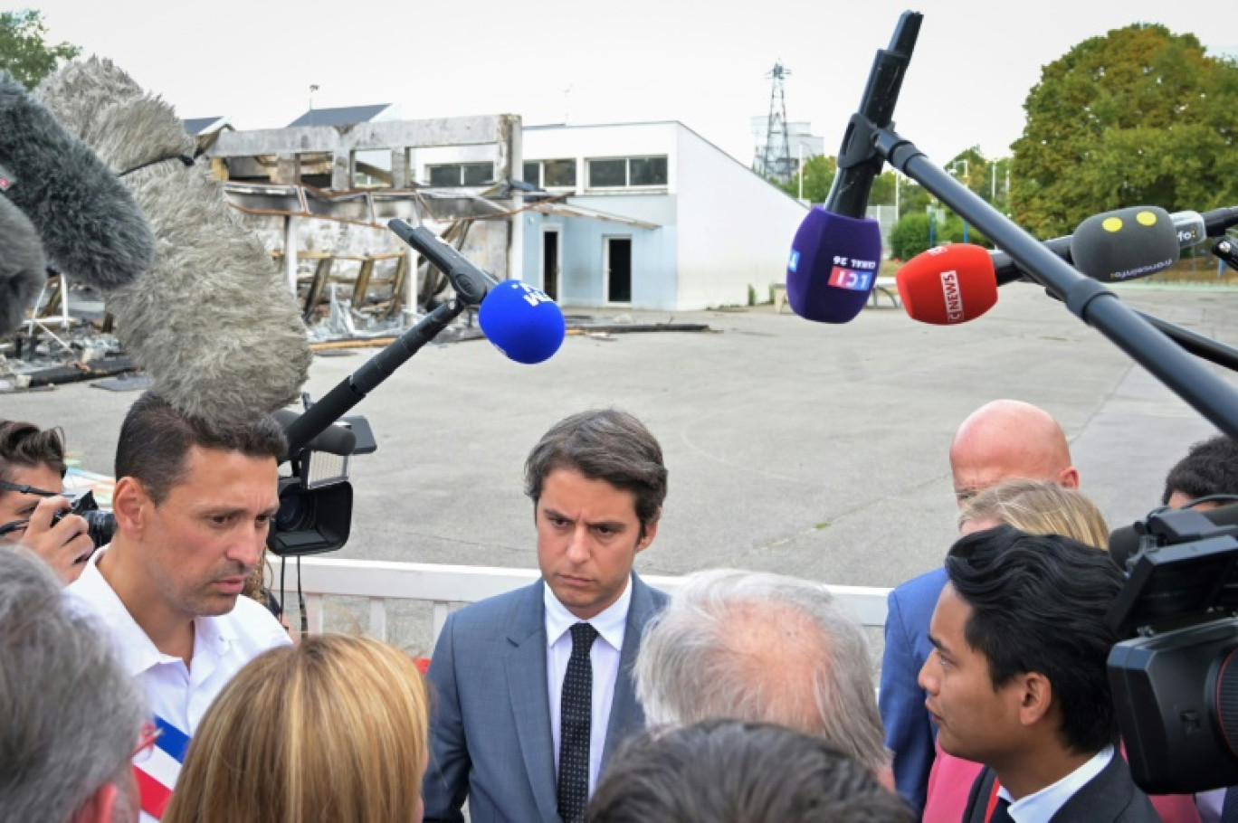 Le nouveau ministre de l'Education Gabriel Attal en déplacement le 21 juillet 2023 à La Verrière, dans les Yvelines, avec l'école du Bois de l'Etang, incendiée pendant les émeutes, en arrière-plan © Alain JOCARD