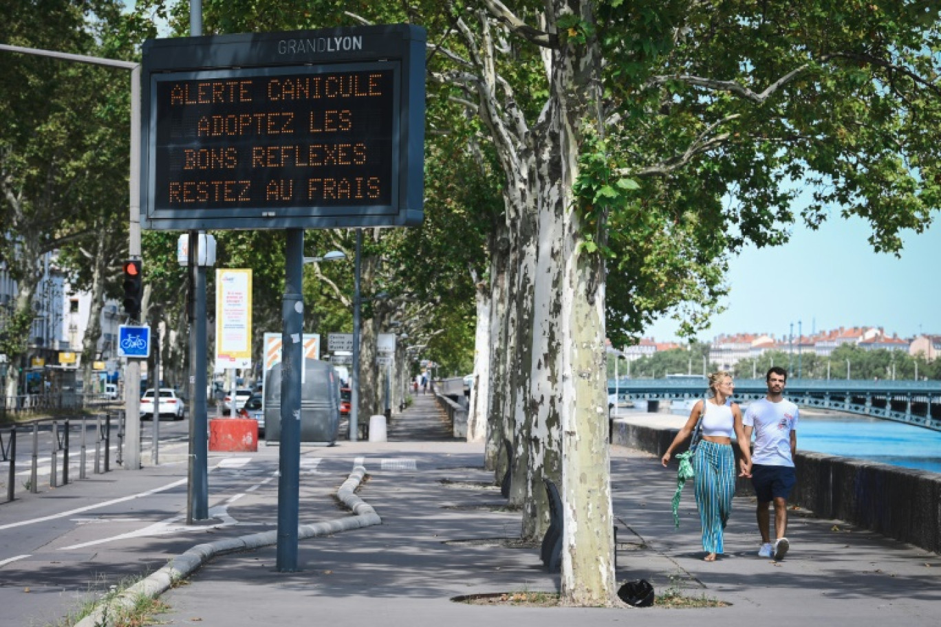 Des piétons à prpximité d'un panneau municipal alertant de la canicule en cours, le 18 août 2023 à Lyon © OLIVIER CHASSIGNOLE