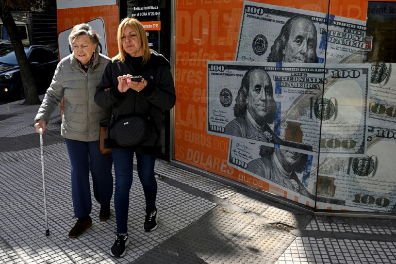 Des femmes passent devant une image de billets de cent dollars, à Buenos Aires le 14 août 2023 © Luis ROBAYO