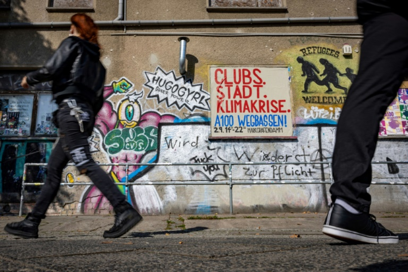 Des personnes passent devant le slogan "Des clubs au lieu d'une crise climatique" inscrit sur un mur à côté du club "About Blank" à Ostkreuz, Berlin Est, le 1er septembre 2023 © Odd ANDERSEN