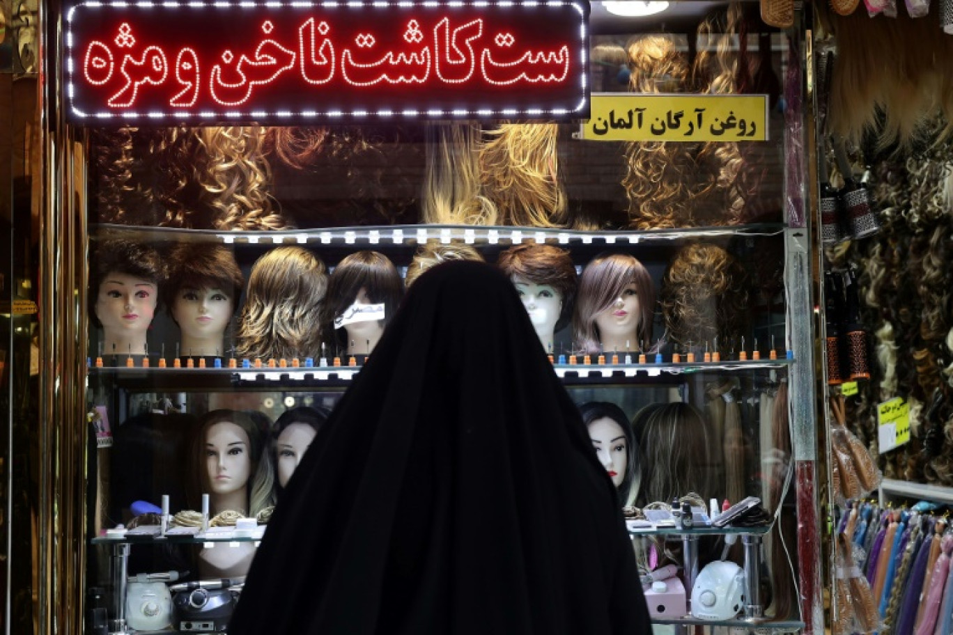 Une femme voilée regarde une vitrine dans une zone commerciale de Téhéran, le 21 février 2023 © ATTA KENARE