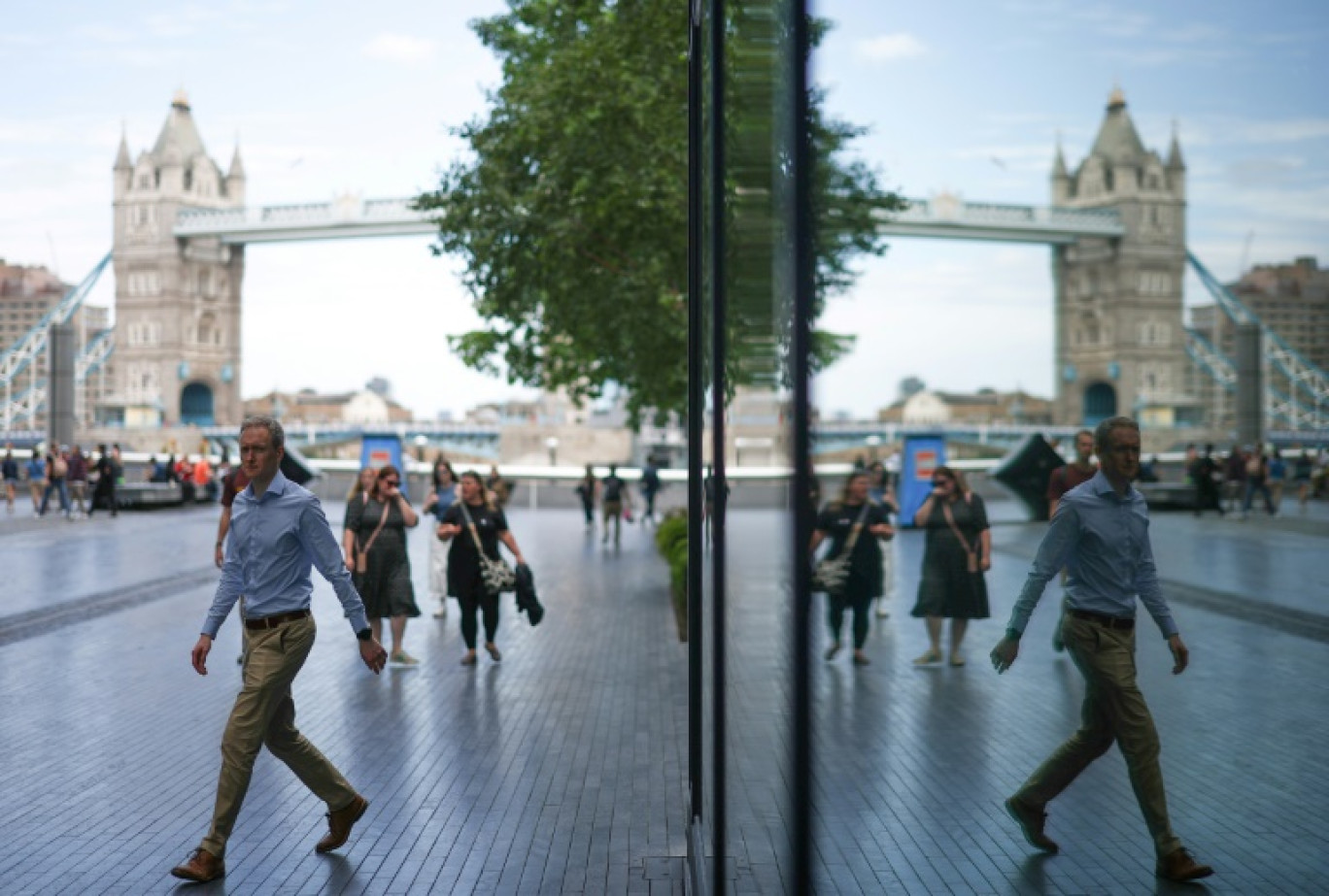 Des passants se reflètent sur un bâtiment vitré dans le quartier de Southbank, près du London Bridge enjambant la Tamise, à Londres, le 14 août 2023 © HENRY NICHOLLS