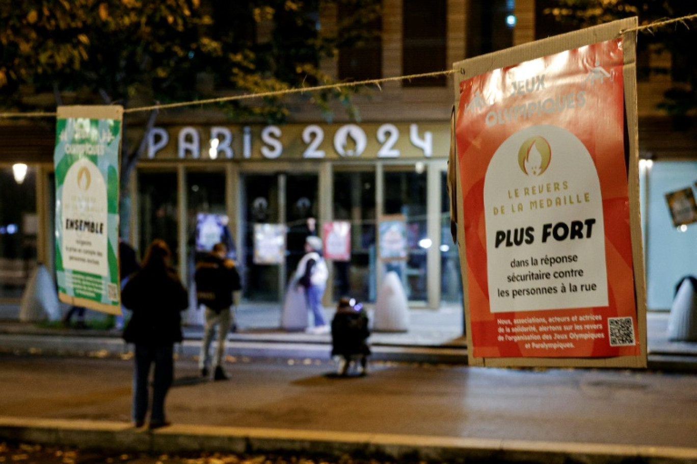 Des militants du collectif "Le revers de la médaille" accrochent des affiches sur des arbres situés devant le bâtiment du comité d'organisation des Jeux olympiques, le 30 octobre 2023 à Saint-Denis, en Seine-Saint-Denis © Geoffroy VAN DER HASSELT