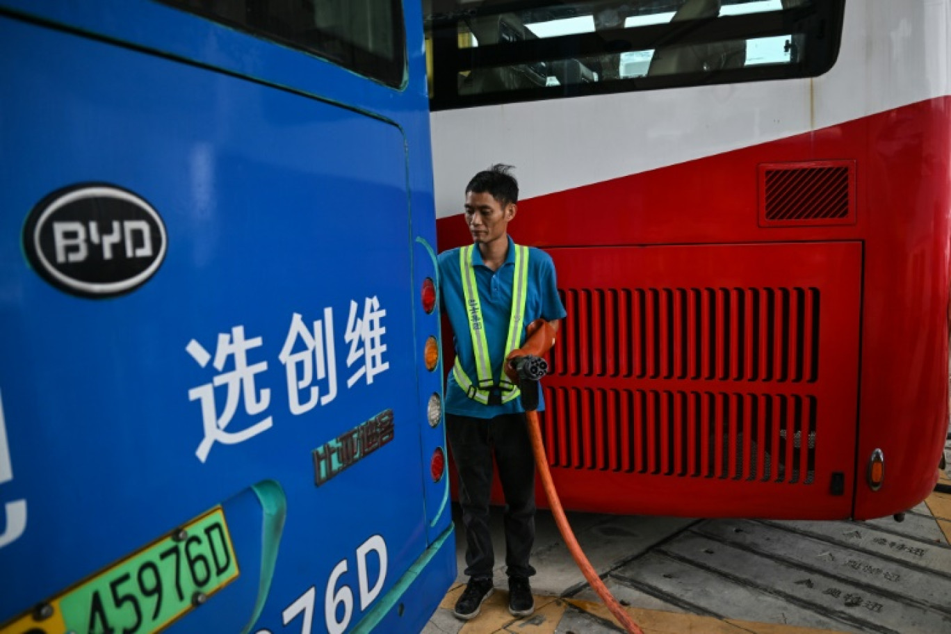 Un employé débranche le câble de recharge d'un bus électrique dans une  station de recharge à Shenzhen, le 18 octobre 2023 dans le sud de la Chine © Hector RETAMAL