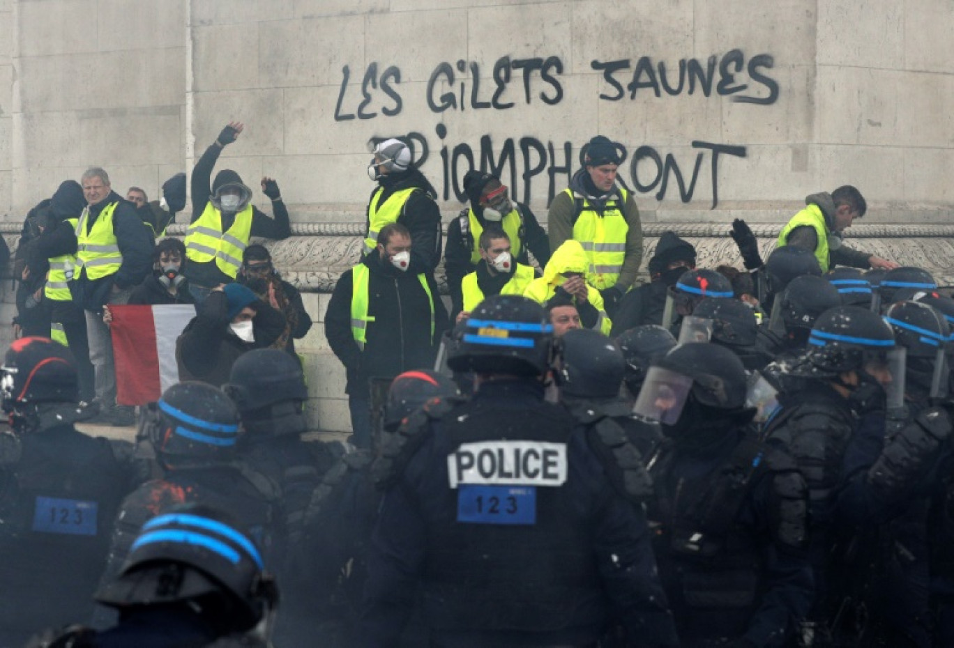 Des manifestants se tiennent devant l'Arc de Triomphe après avoir écrit sur un mur du monument "Les gilets jaunes triompheront" lors d'affrontements avec les policiers anti-émeutes l 1er décembre 2018 à Paris © Geoffroy VAN DER HASSELT