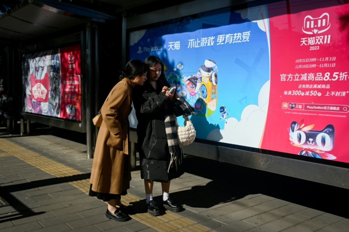 Deux habitantes de Pékin le 11 novembre 2023 devant une affiche faisant la promotion de la "Fête des célibataires", grande opération de soldes en Chine qui s'achève cette année dans un contexte de consommation atone. © WANG Zhao