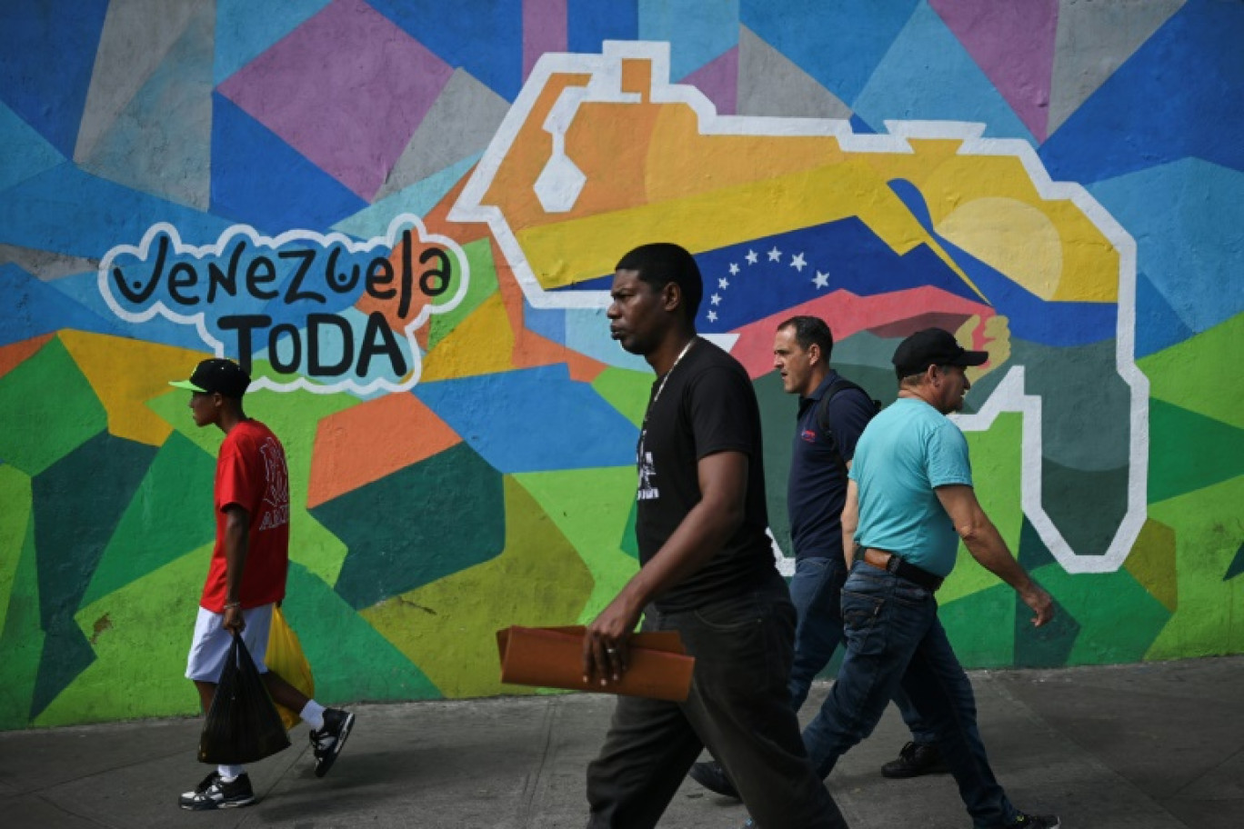 Des personnes passent devant une fresque murale faisant campagne pour un référendum demandant aux Vénézuéliens d'envisager l'annexion de la région de l'Essequibo administrée par le Guyana voisin, à  Caracas, le 28 novembre 2023 © Federico PARRA