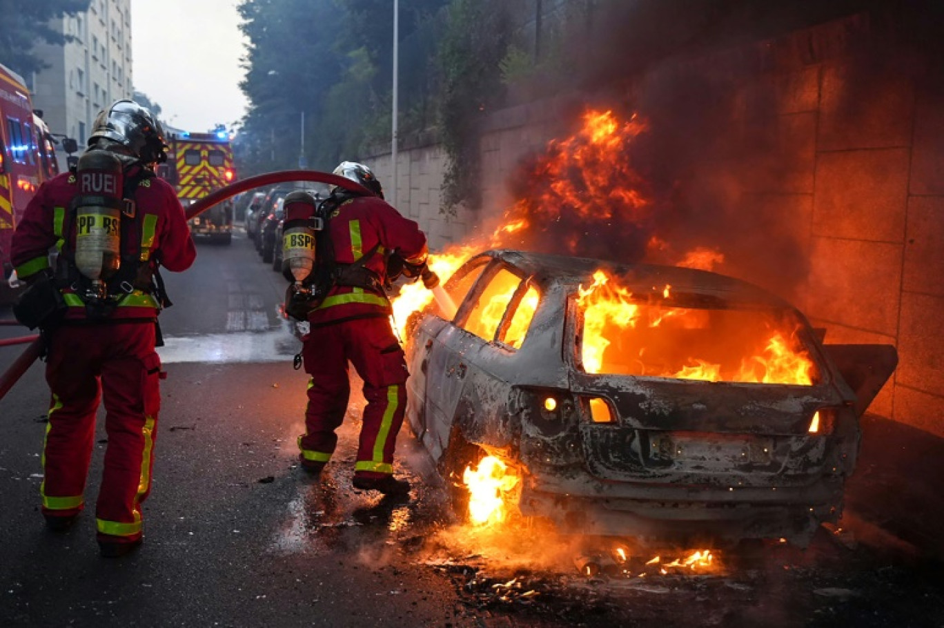 Des pompiers tentent d'éteindre une voiture en feu en marge d'une manifestation à Nanterre,  théâtre d'incidents en soirée, le 27 juin 2023 © Zakaria ABDELKAFI