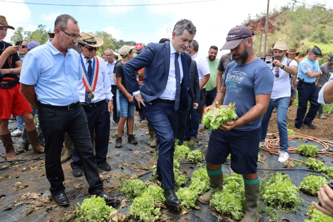 Le ministre français de l'Intérieur Gérald Darmanin (c) inspecte une exploitation agricole après le passage du cyclone Belal au Tampon, sur l'île de La Réunion, le 17 janvier 2024 © SLY