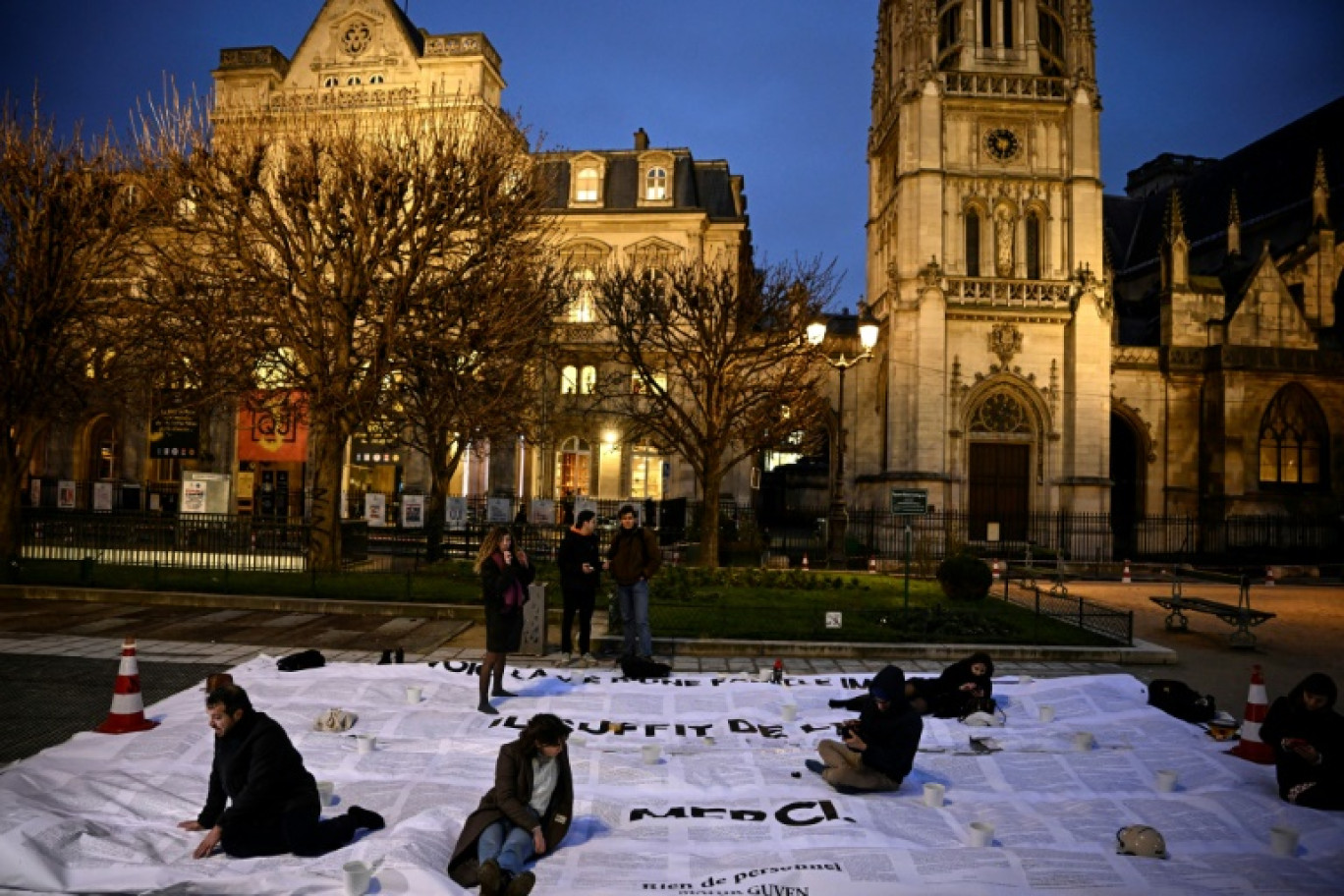 Des bénévoles aident l'écrivain franco-turc Mahir Guven (g) à installer un collage géant tiré de son livre "Rien de personnel" pour protester contre la loi sur l'immigration, le 23 janvier 2024 à Paris © JULIEN DE ROSA