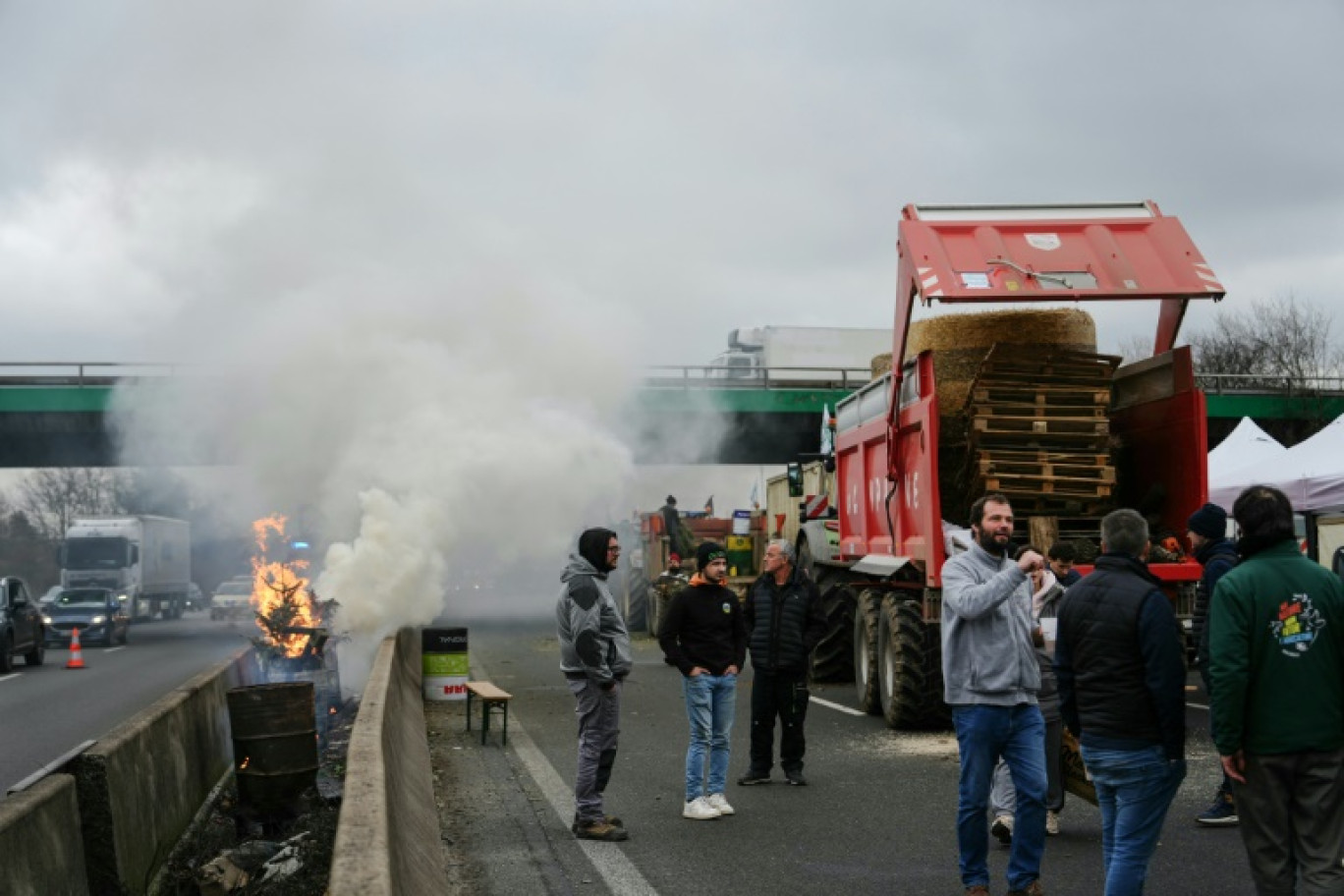 Des manifestants se tiennent à côté d'un feu dans un baril et de tracteurs bloquant l'autoroute A15 près d'Argenteuil, au nord-ouest de Paris, le 30 janvier 2024 © Dimitar DILKOFF