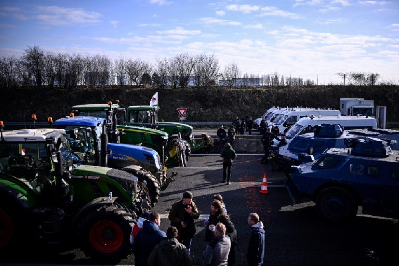 Des agriculteurs en tracteur font face à des fourgons et véhicules blindés de la gendarmerie sur l'autoroute A1 près de l'aéroport Roissy-Charles-de-Gaulle, au nord-ouest de Paris, le 31 janvier 2024 © JULIEN DE ROSA