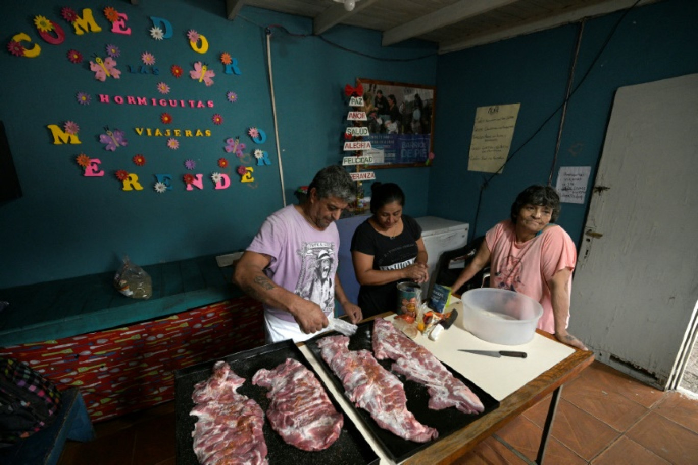 Marcelo Lopez (g), cuisinier de la soupe populaire "Las Hormiguitas Viajeras", prépare du porc avec des pâtes, aidé par son assistante Angelina Escobar (c), et sa femme Norma Olea à Loma Hermosa, dans la province de Buenos Aires, le 9 février 2024 en Argentine © JUAN MABROMATA