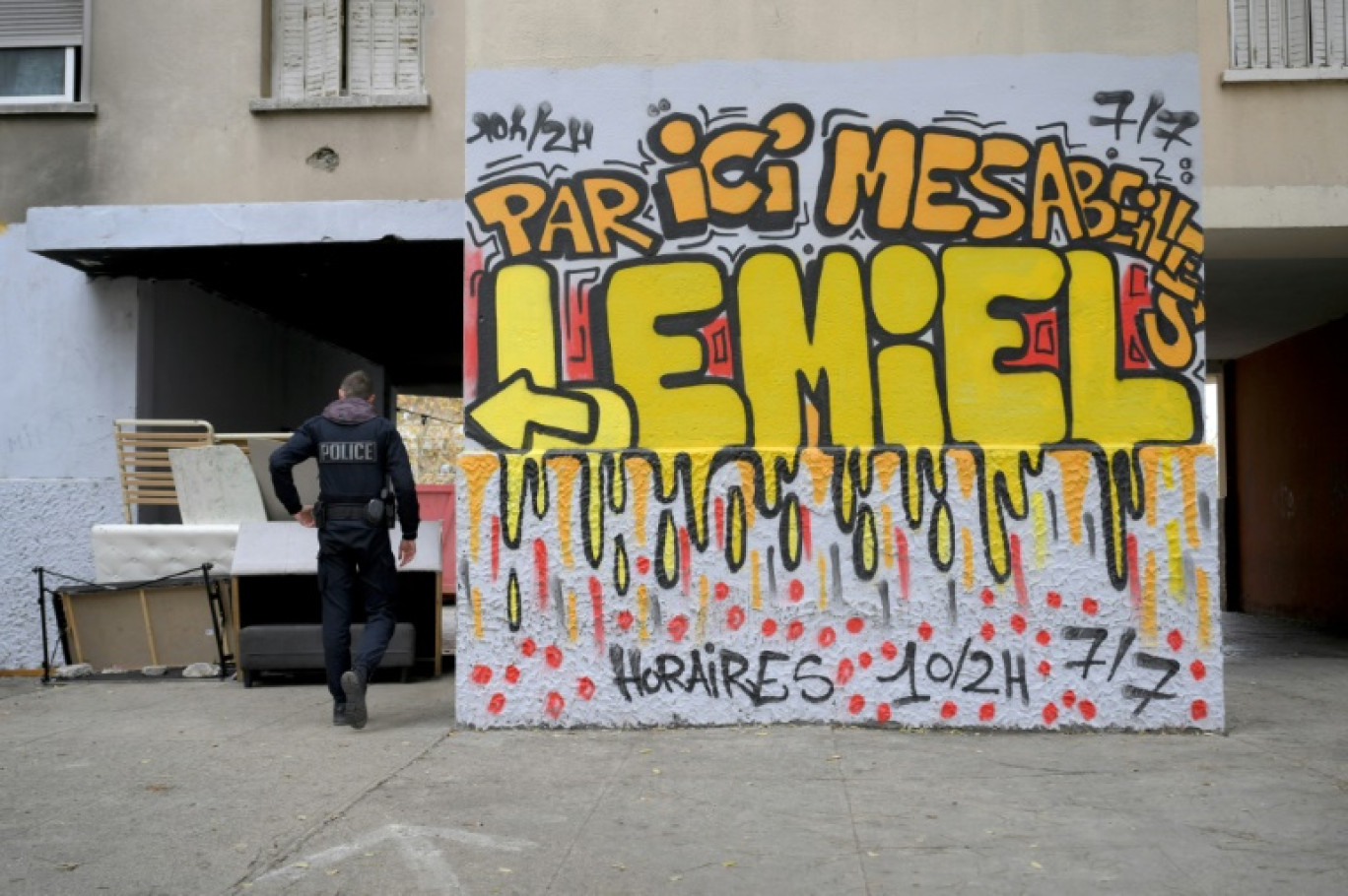 Un policier de la 14e Brigade BST, spécialisée dans le trafic de drogue, à côté un graffiti "Par ici mes abeilles vous trouverez du miel ouvert 10/2h 7j/7" dans un point de deal de la cité des Rosiers, dans les quartiers nord de Marseille, le 1er décembre 2023 © Nicolas TUCAT