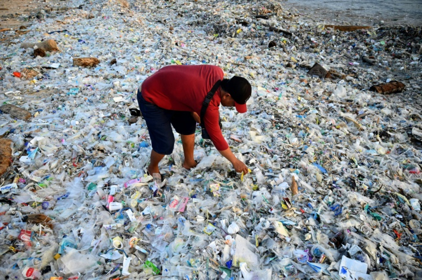 Un homme fouille dans des ordures et déchets plastiques échoués sur la plage de Kedonganan, sur l'île indonésienne de Bali, le 19 mars 2024 © SONNY TUMBELAKA