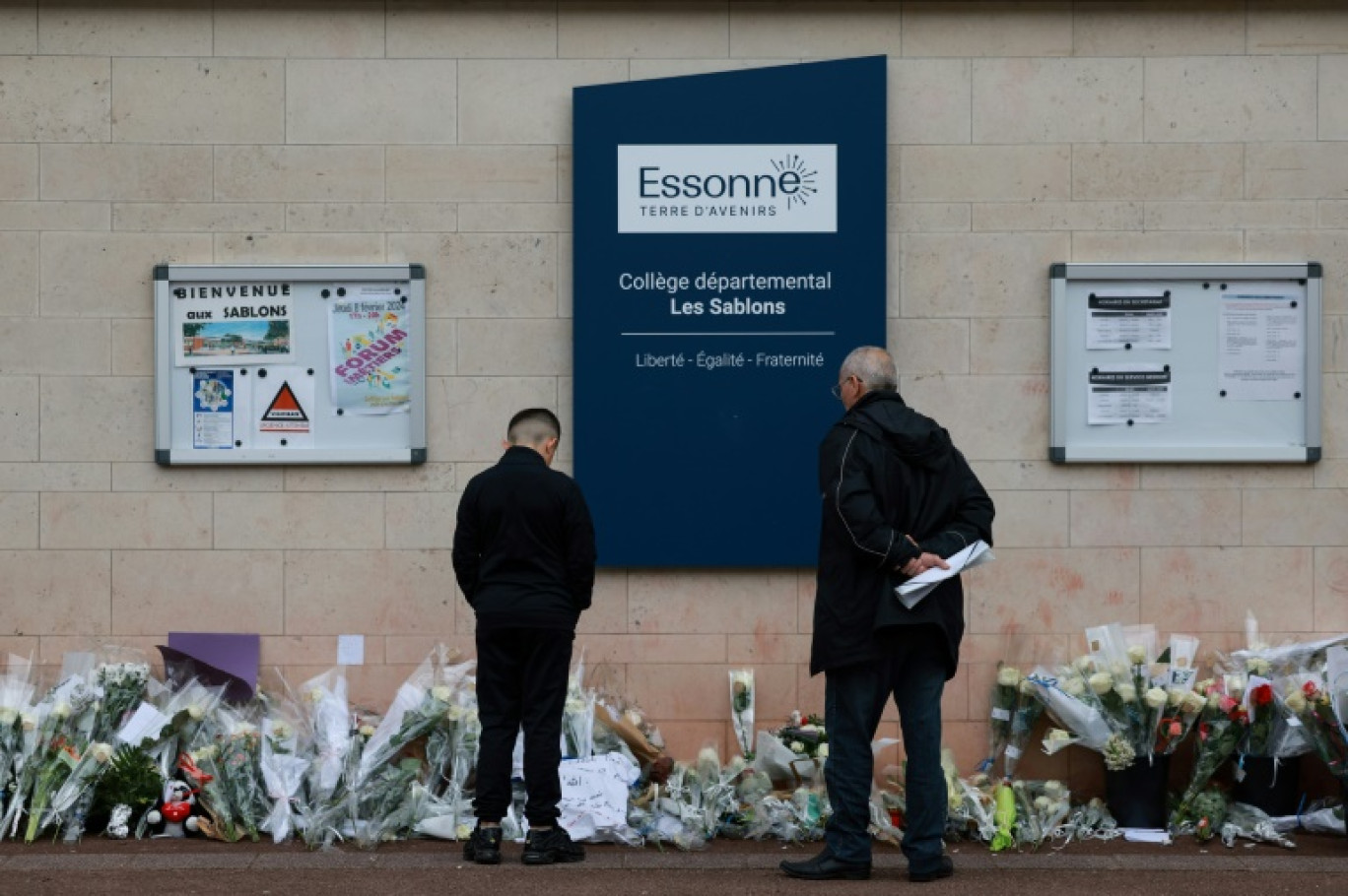 Des habitants regardent les fleurs déposées devant le collège des Sablons à Viry-Châtillon, en Essonne, le 7 avril 2024 © Emmanuel Dunand