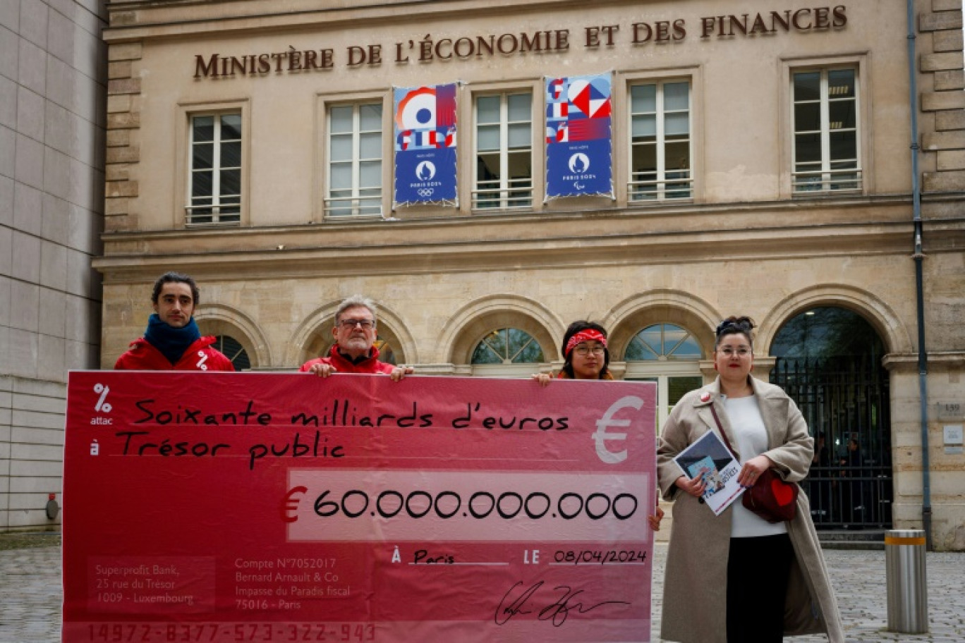 Des militants d'Attac tiennent un "chèque" géant de 60 milliards d'euros, ce facsimilé représentant, selon eux, le déficit public qui pourrait être comblé en taxant les très riches plutôt qu'en taillant dans les dépenses, devant le ministère de l'Economie et des Finances, le 8 avril 2024 © Dimitar DILKOFF