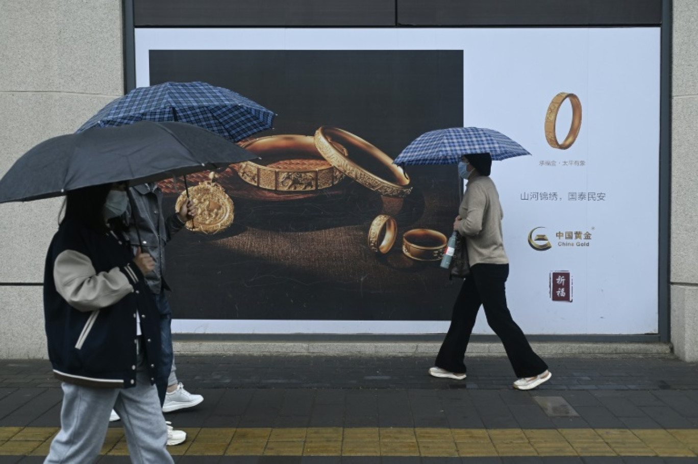 Des passants avec des parapluies marchent devant un panneau publicitaire à Pékin le 10 avril 2024 © WANG Zhao