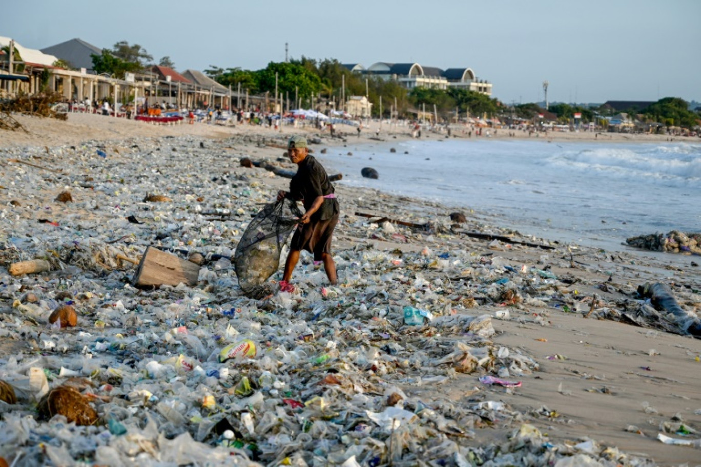 Un homme ramasse des objets recyclables pour les vendre au milieu de plastiques et d'autres débris échoués sur la plage de Kedonganan, dans la zone touristique de Kuta, sur l'île de Bali, en Indonésie, le 19 mars 2024 © SONNY TUMBELAKA