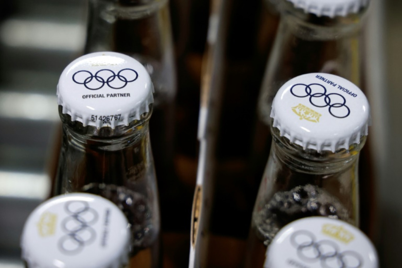 Le logo des Jeux olympiques sur des capsules de bouteilles de bière sans alcool Corona Cero, sur une ligne de production à la brasserie Anheuser-Busch InBev (AB InBEV), le 23 avril 2024 à Louvain, en Belgique © Kenzo TRIBOUILLARD