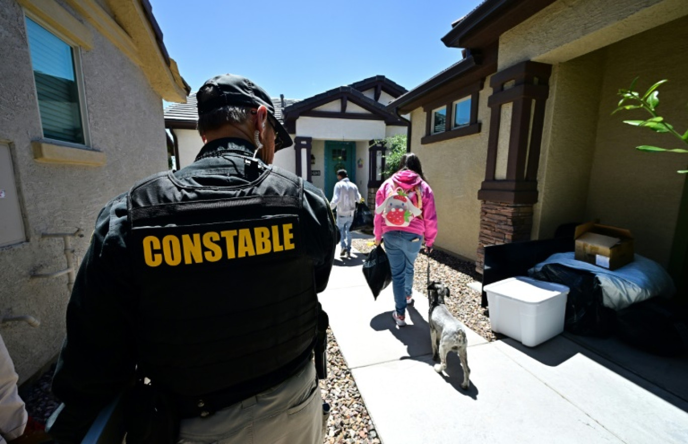 Lennie McCloskey, agent de police de la circonscription judiciaire de Manistee, dans le comté de Maricopa, observe une famille qui vient d'être expulsée, à Phoenix (Arizona), aux Etats-Unis, le 15 avril 2024 © Frederic J. BROWN