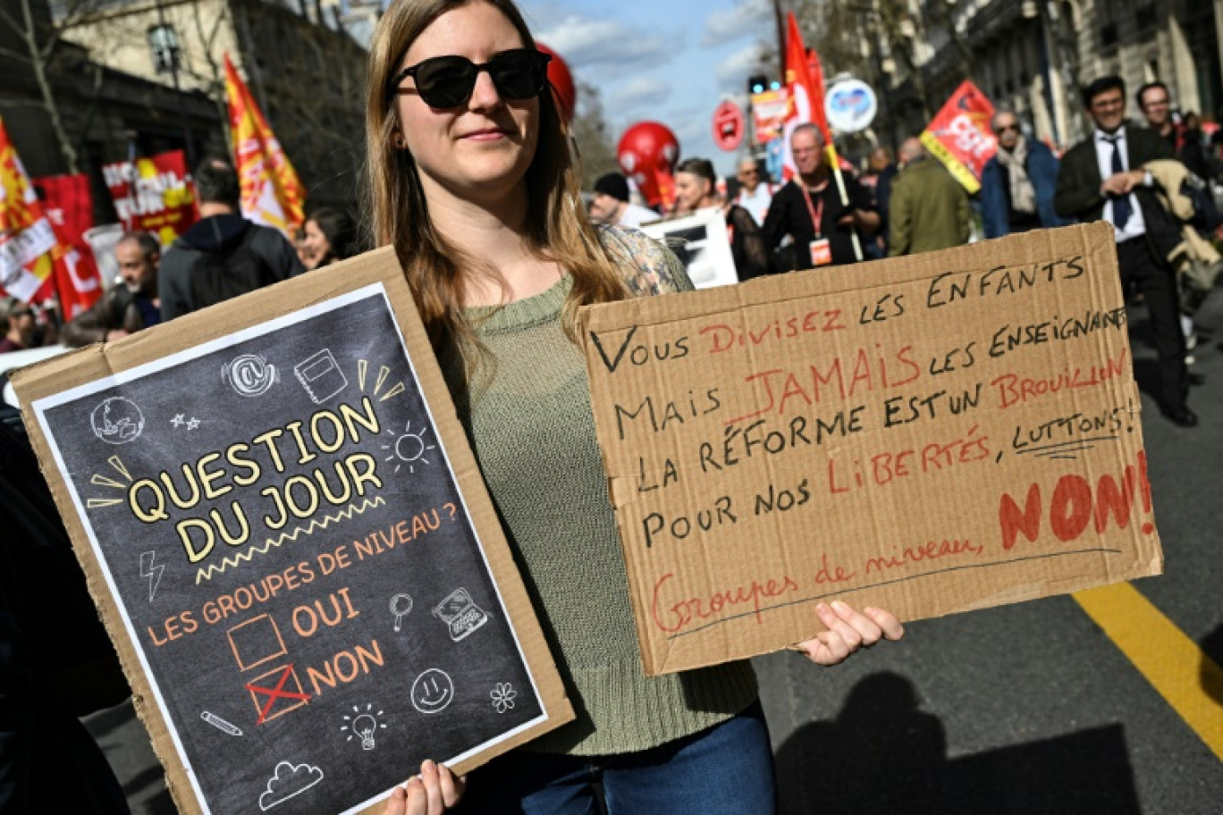 Une personne tient deux pancartes contre les groupes de niveau lors d'une manifestation le 19 mars 2024 à Paris © Bertrand GUAY