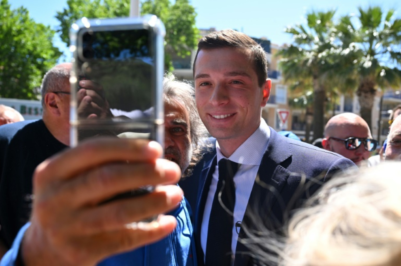 Jordan Bardella, président du RN et tête de liste aux élections européennes, pose pour un selfie avec un partisan lors d'une visite de campagne dans un marché en plein air de la ville de Sainte-Maxime, le 31 mai 2024 © Nicolas TUCAT