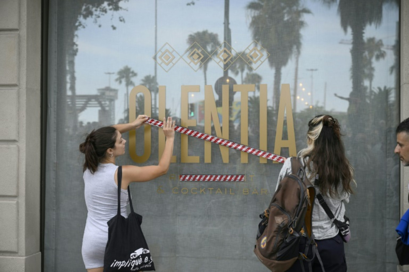 Des manifestants installent un ruban sur la vitrine d'un magasin pour protester contre le surtourisme, le 6 juillet 2024 à Barcelone © Josep LAGO