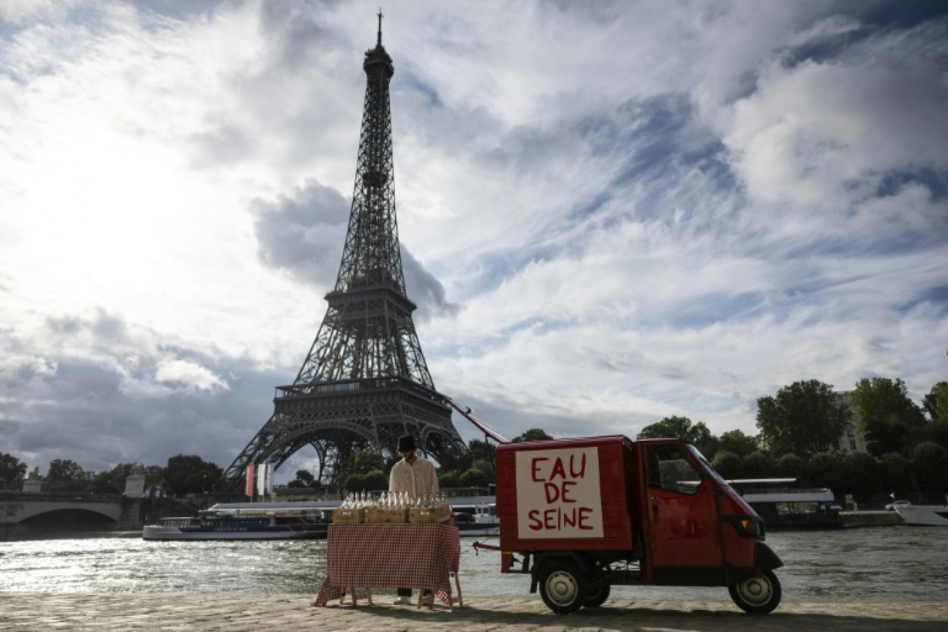 Un acolyte de l'artiste de rue James Colomina vend de l'eau en bouteille de la Seine devant la Tour Eiffel, à Paris le 10 juillet 2024 © Olympia DE MAISMONT