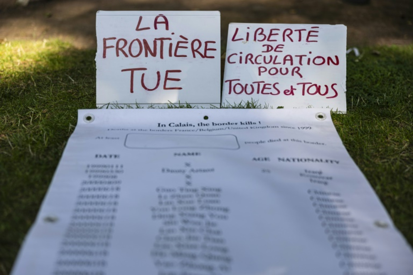 Hommage aux migrants morts lors d'une tentative de traversée de la Manche dont les noms sont inscrits sur un longue feuille de papier, le 19 juillet 2024 à Calais © Sameer Al-DOUMY