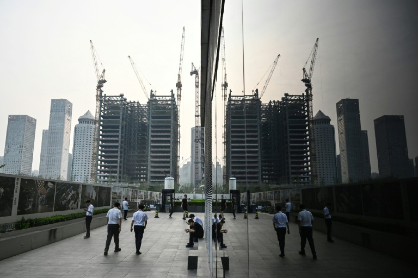 Des employés de bureau marchent le long du mur d'un chantier de construction dans le quartier central des affaires de Pékin, le 11 juillet 2024 © GREG BAKER