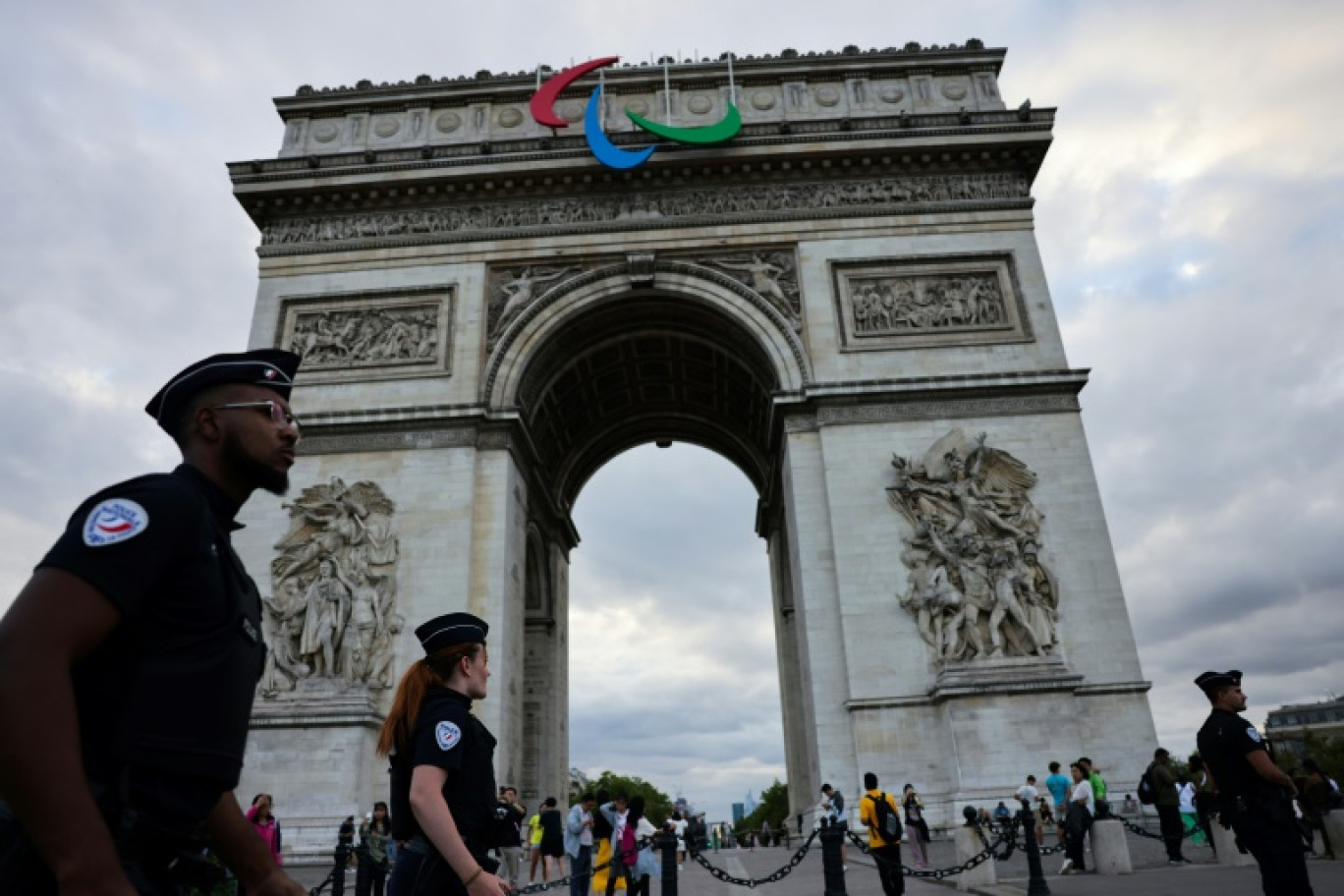 Des policiers passent devant l'Arc de triomphe arborant le sigle des Jeux paralympiques de Paris, le 22 juillet 2024 © AHMAD GHARABLI