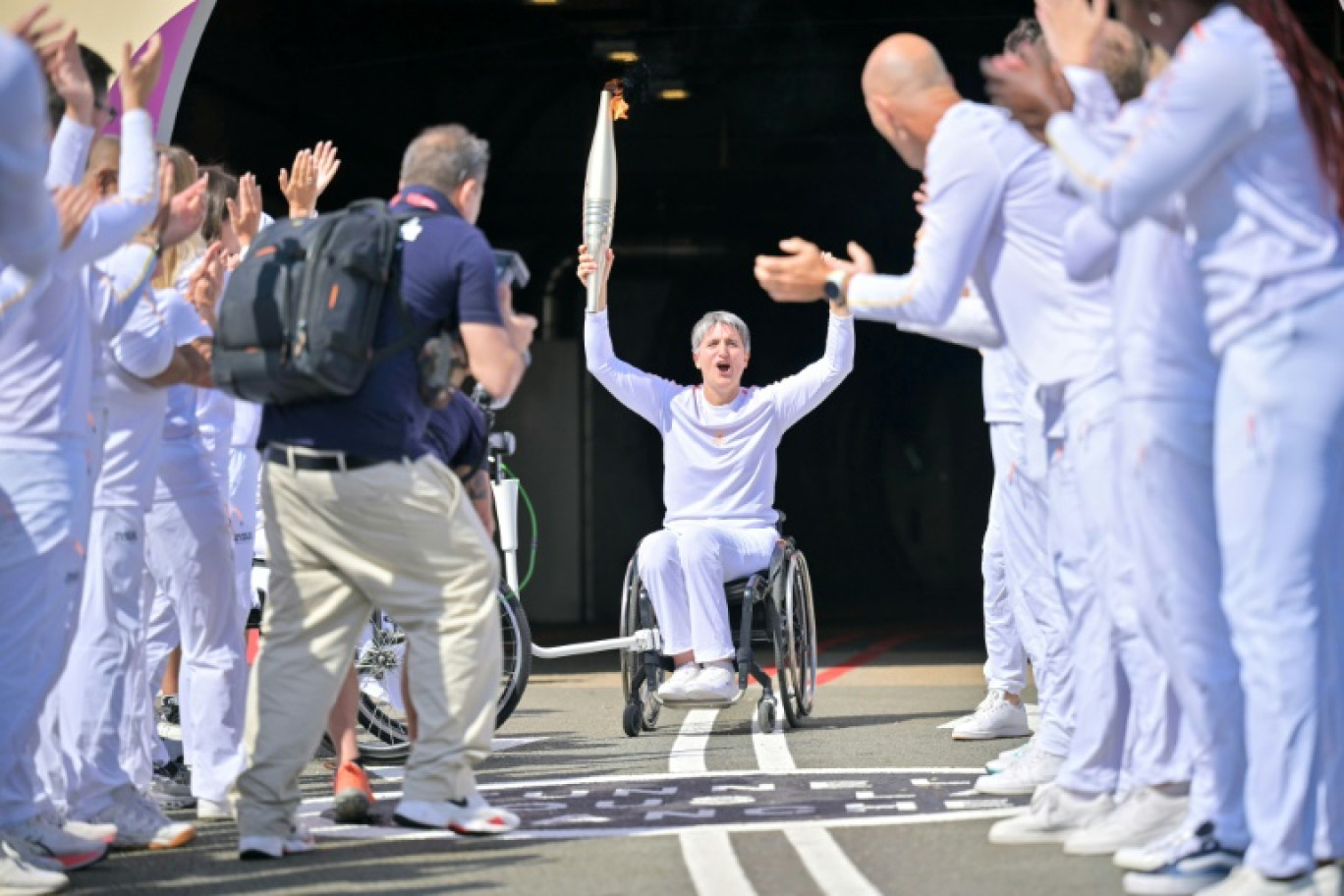 Emmanuelle Assmann, médaillée en escrime-fauteuil, brandit la flamme paralympique 
au terme d'une traversée inédite par le tunnel sous la Manche, le 25 août 2024 à Coquelles dans le Pas-de-Calais © LOU BENOIST