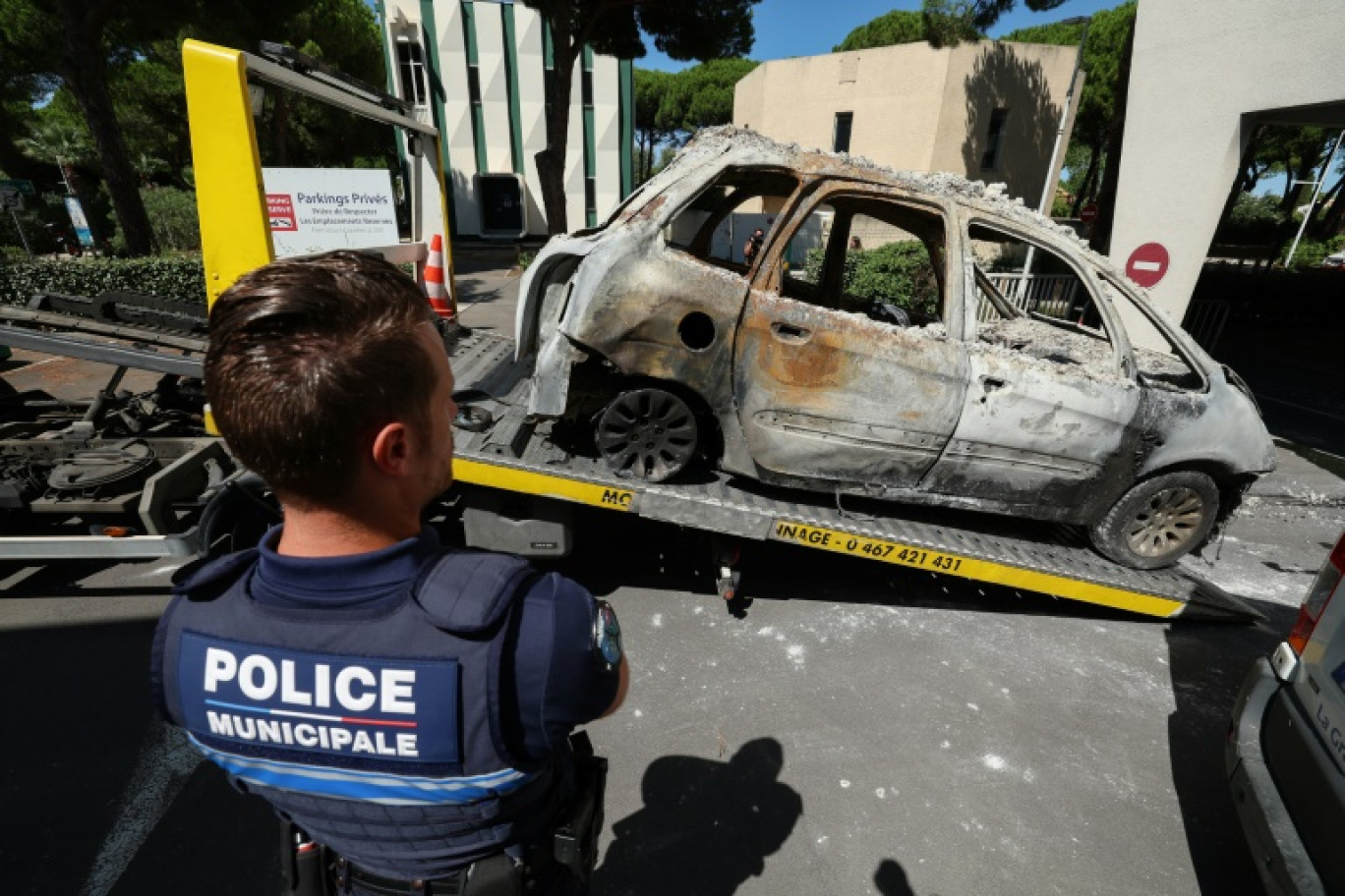 Un policier devant une voiture brûlée placée sur la plateforme d'un véhicule de remorquage à La Grande Motte, deux jours après l'attentat contre une synagogue, le 26 août 2024 dans l'Hérault © Pascal GUYOT