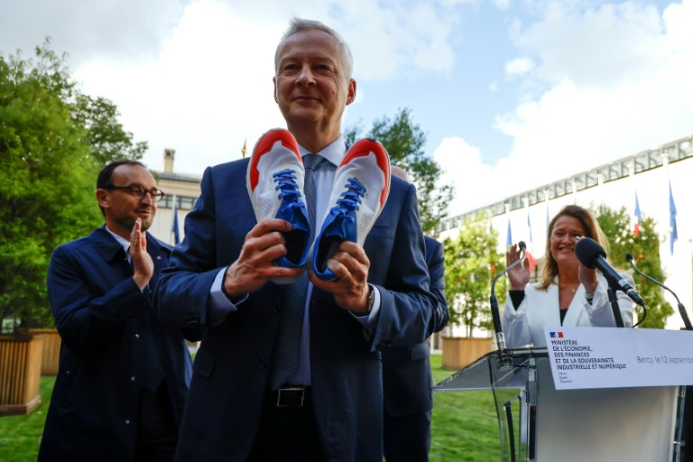 Le ministre démissionnaire de l'Economie Bruno Le Maire (c) montre la paire de baskets offerte par ses collègues lors d'une conférence à Bercy, le 12 septembre 2024 à Paris © Ludovic MARIN