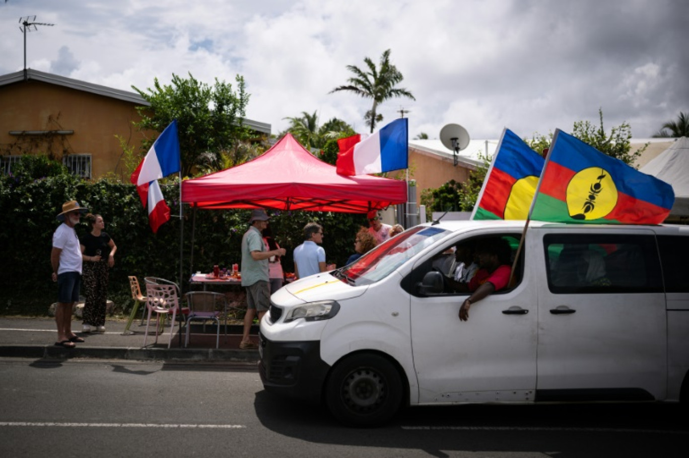 Des habitants célèbrent l'anniversaire de la prise de possession de la Nouvelle-Calédonie par la France, tandis qu'une voiture occupée par des indépendantiste passe dans une rue de Nouméa, dans le quartier de Magenta, le 24 septembre 2024 © SEBASTIEN BOZON