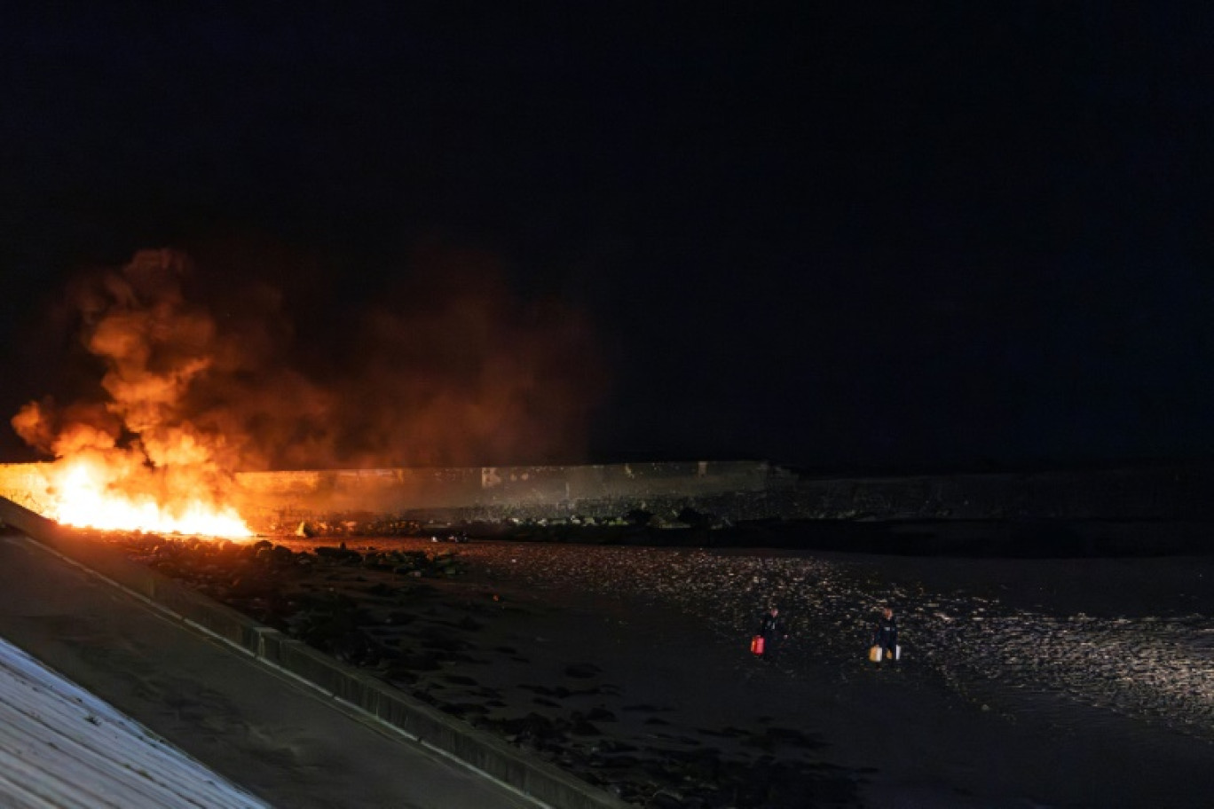 Des policiers éloignent des bidons d'essence d'un canot en feu sur la plage du Portel (Pas-de-Calais) le 21 septembre 2024 © Sameer Al-DOUMY