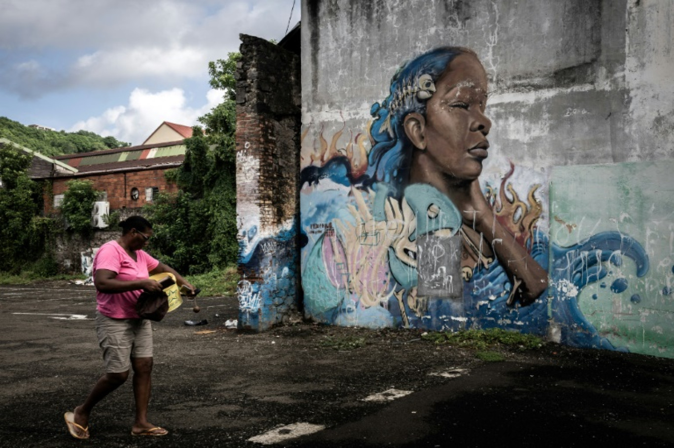 Une femme passe devant un graffiti dans le centre-ville de Fort-de-France, en Martinique, au milieu des émeutes sur la hausse des prix, le 14 octobre 2024 © PHILIPPE LOPEZ