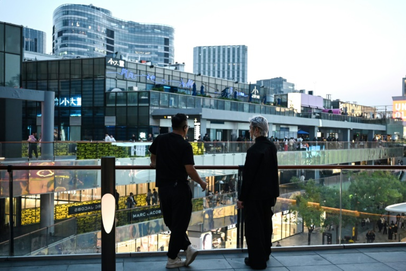 Deux hommes se tiennent debout dans un quartier commercial, à Pékin, le 4 octobre 2024. © GREG BAKER