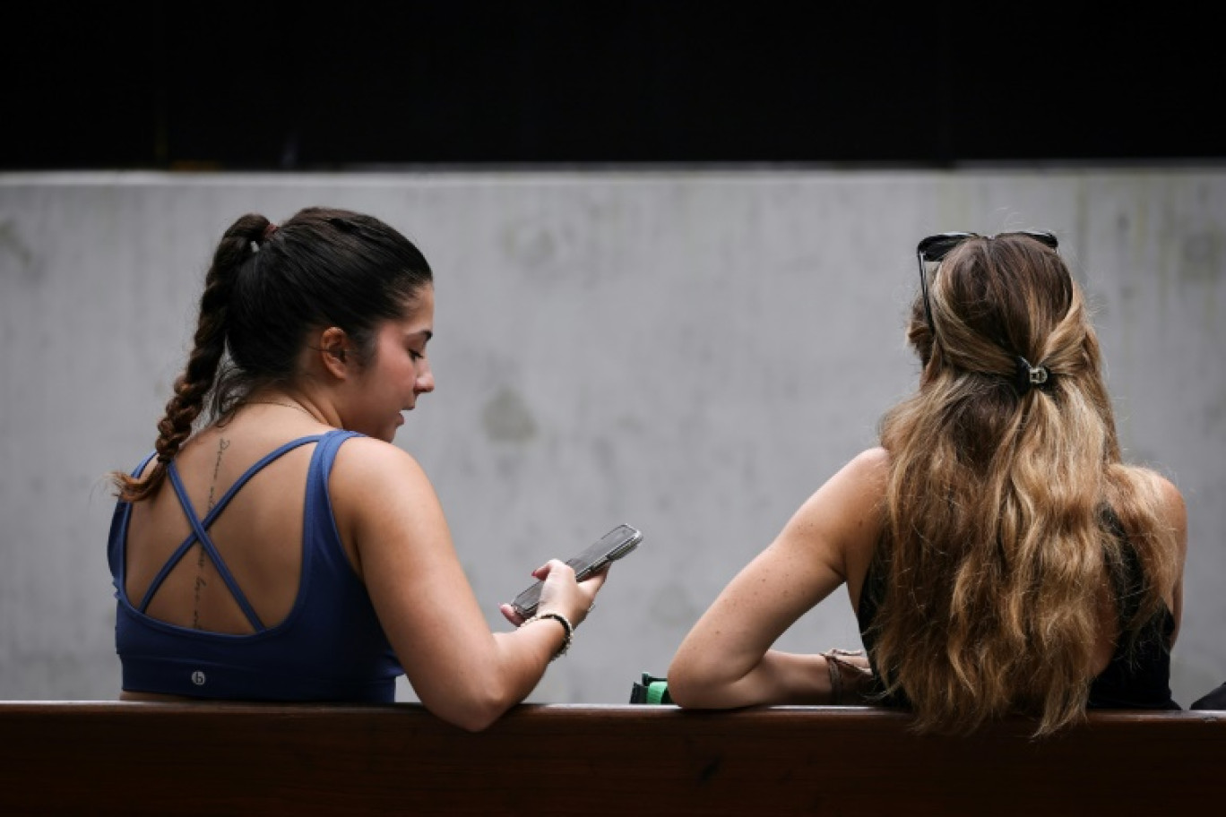 Deux jeunes femmes sur un banc à Sydney regardent un téléphone mobile, le 7 novembre 2024 © DAVID GRAY