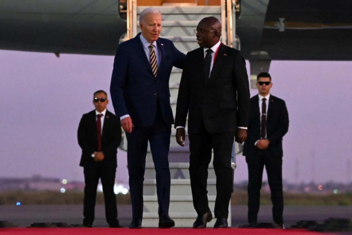 Le président américain Joe Biden (g) marche à côté du ministre angolais des Affaires étrangères Tete Antonio à son arrivée à l'aéroport international Quatro de Fevereiro de Luanda, le 2 décembre 2024 © ANDREW CABALLERO-REYNOLDS