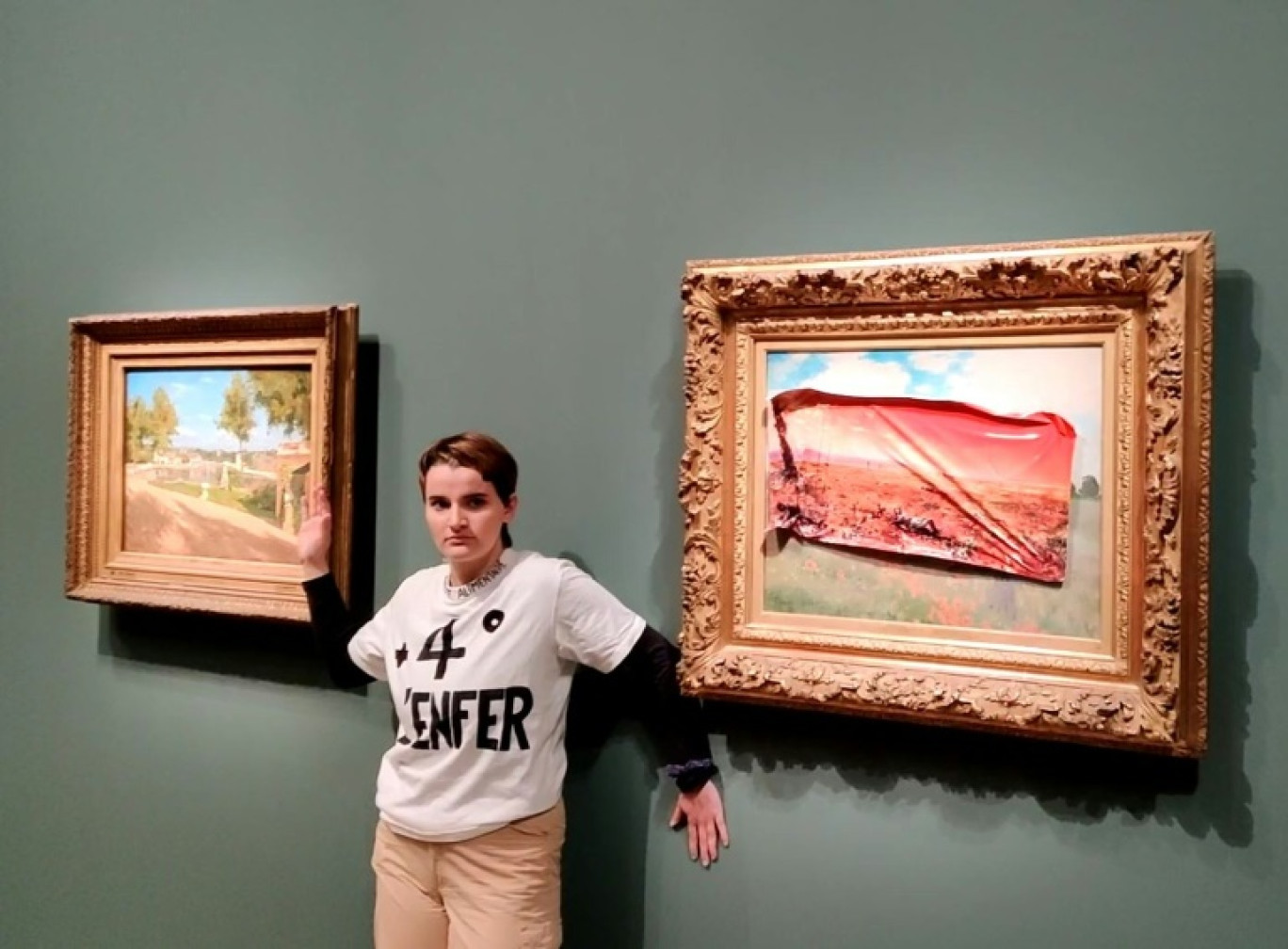 Photo diffusée le 1er juin 2024 par le collectif Riposte Alimentaire d'une de ses militantes portant un tee-shirt "+4° l'enfer" devant le tableau de Claude Monet "Les Coquelicots" recouvert d'un autocollant représentant la même scène en l'an 2100, ravagée par les flammes et la sécheresse, au Musée d'Orsay, à Paris © Handout