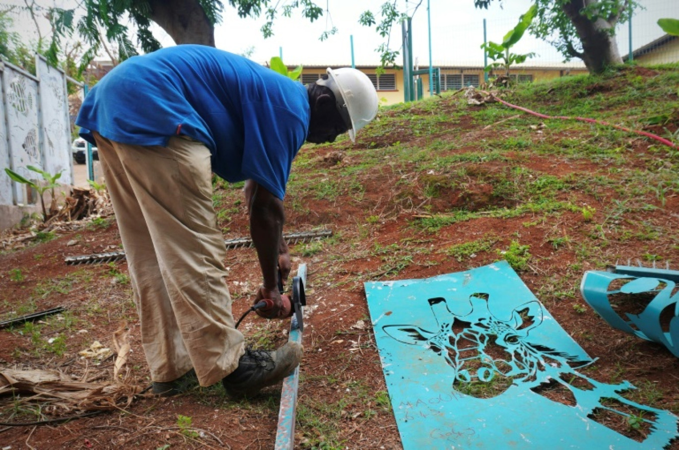 Un ouvrier réutilise des débris métalliques le 25 janvier 2025 pour réparer le portail d'une école primaire à Passamainty, dans un quartier de Mamoudzou à Mayotte, dévasté par le cyclone Chido en décembre © Marine GACHET