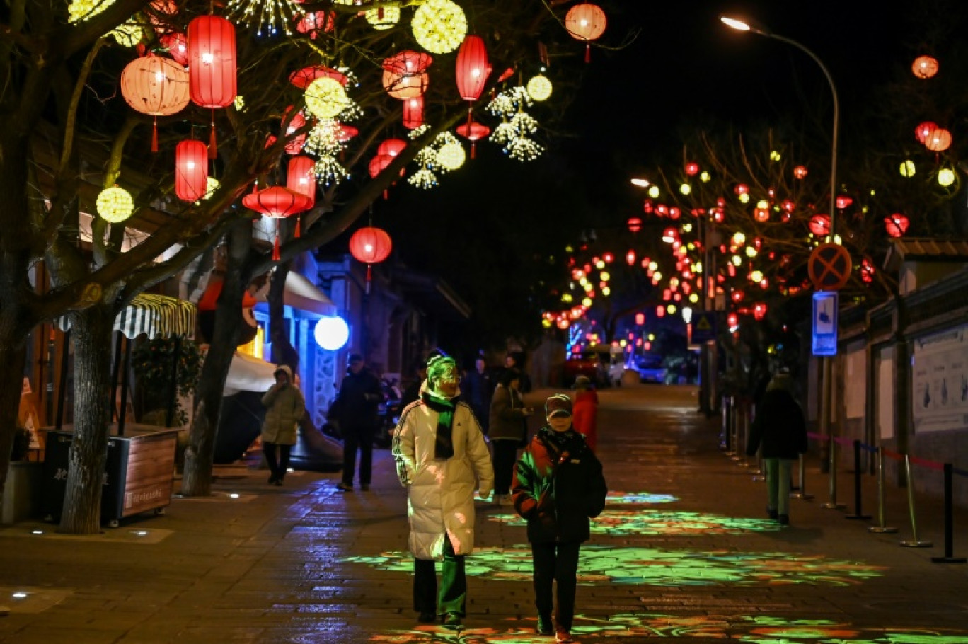 Des piétons dans une rue décorée de lanternes  à la veille de la nouvelle année lunaire du serpent à Pékin, le 28 janvier 2025 © GREG BAKER