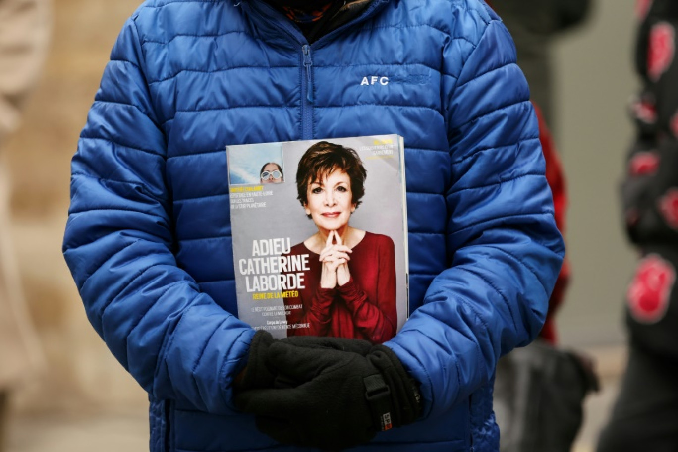 Un participant aux funérailles tient la première page d'un magazine montrant un portrait de l'ancienne présentatrice météo de la télévision Catherine Laborde, le jour de sa cérémonie funéraire, à l'église Saint-Roch à Paris le 6 février 2025 © Alain JOCARD