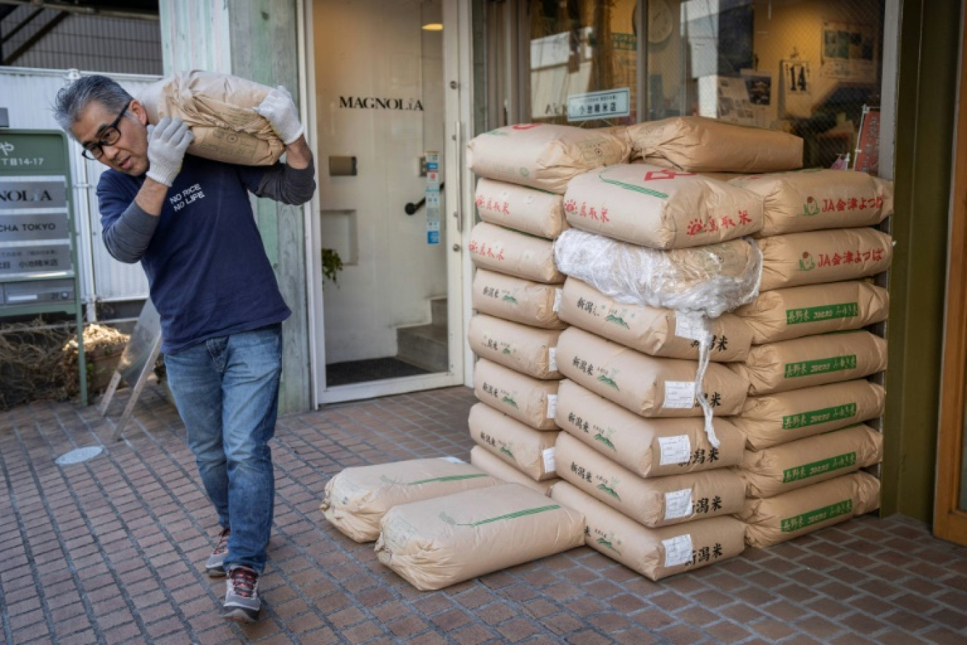 Le propriétaire du magasin de riz Tadao Koike porte un sac de riz dans son magasin à Tokyo, le 14 février 2025 © Yuichi YAMAZAKI