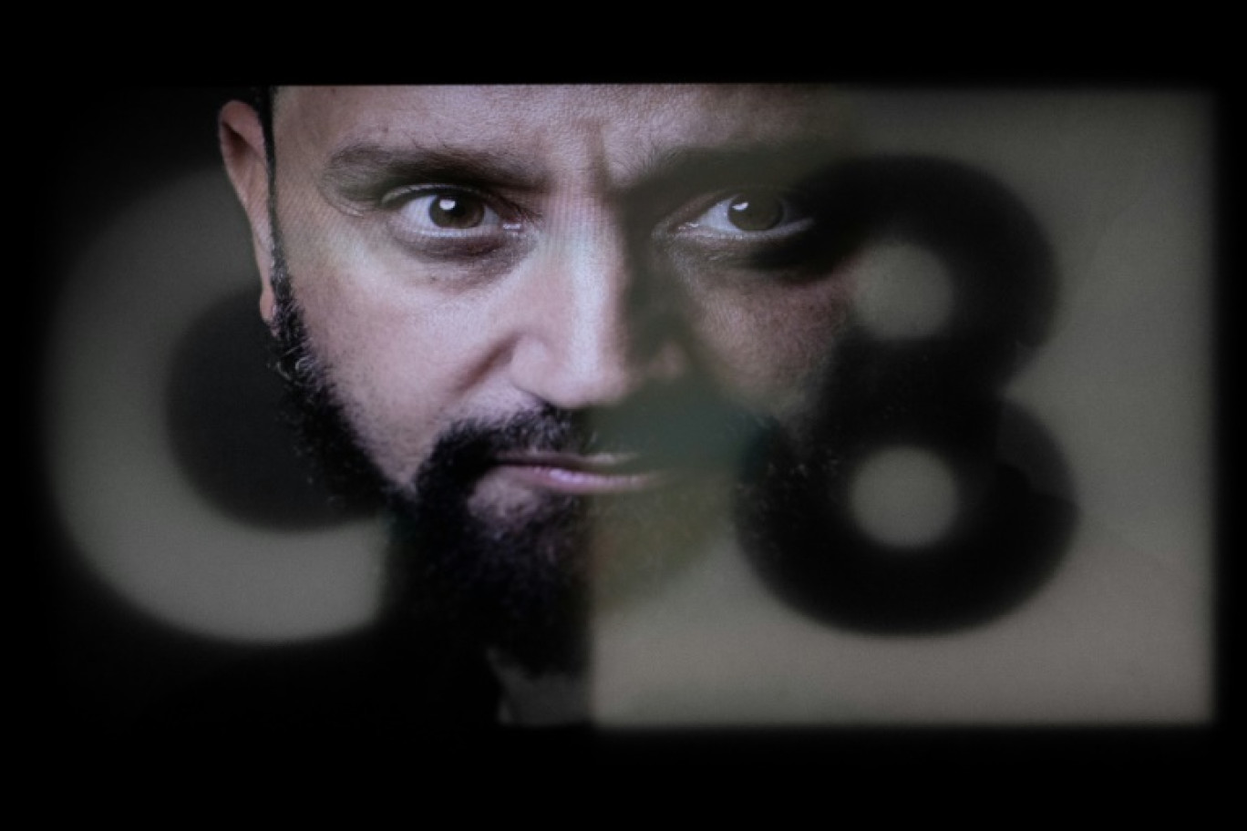 Un portrait de l'animateur de télévision français Cyril Hanouna reflété dans un écran affichant le logo de la chaîne de télévision française C8, à Paris le 28 février 2025 © JOEL SAGET