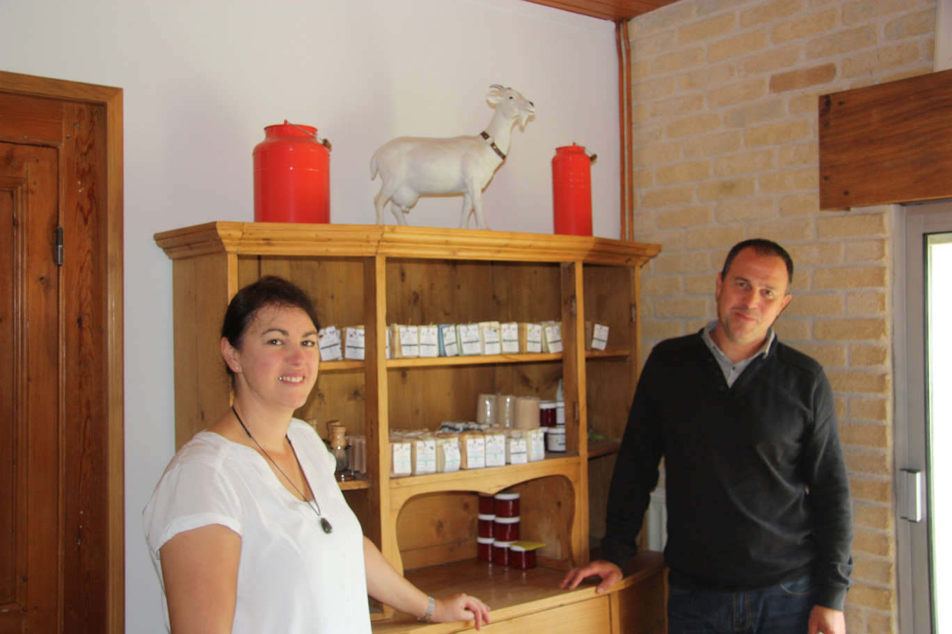 Claudia et Sylvain Janquin devant un présentoir exposant leurs savons. La présence de la chèvre et les deux pots symbolise l'emploi du lait de chèvre dans la fabrication de leurs savons.